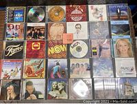 Photo showing 30 assorted music CDs arranged in 5 rows of 6, various artists and album covers visible including Fame soundtrack and other albums.