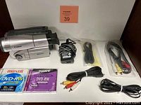 Canon ES8400V 8mm camcorder with various cables and two DVD-RW discs on a table with a seller's lot number behind