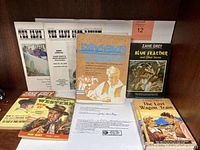 Photo of multiple Zane Grey books, magazines, and notarized letter arranged on a wooden surface.