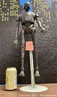 Front view of K-2SO action figure next to soda can for size comparison, figure supported by white display stand.