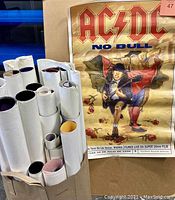 Rolled posters in a container and prominently displayed AC/DC No Bull vintage poster.