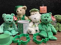 Several Saint Patrick's Day themed Beanie Babies of various sizes and colors, green cookie cutters shaped like shamrocks, a green felt hat, and a white mug with shamrocks and a blessing.
