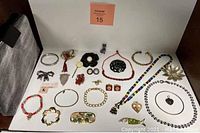 Photo showing an array of vintage jewelry pieces including pendants, bracelets, brooches, necklaces, earrings and an arrowhead pendant arranged next to the black and silver makeup/jewelry case