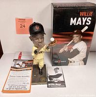 Photo showing Willie Mays bobble head figurine posed catching a baseball and the original box with Willie Mays batting image, plus included card and brochure.