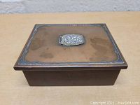 Front view of the rectangular bronze box showing the sterling silver plaque on the lid with decorative engraving.