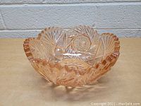 Front angled view of the pink thick glass bowl showing the scalloped edge and intricate pressed glass starburst pattern.