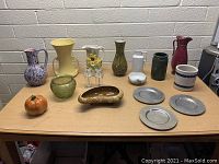 Box lot of assorted pottery and decorative items arranged on table with white brick background.