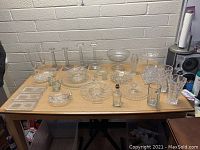 Overview of assorted clear glassware on table including trays, bowls, candle holders, and pitchers.