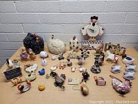 Wide view of lot showing all items on table against a white brick wall including large figurines, clock, salt and pepper shakers, and smaller decorations.