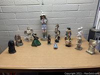 Photo showing 13 assorted figurines on a wooden surface against a brick wall backdrop.