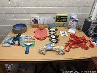 Photo of assorted dog and pet items arranged on a table including toys, grooming tools, books, and dog food items.
