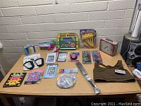 Photo showing large lot of assorted new old stock items on a table including toys, games, crafts, clothing, and accessories.