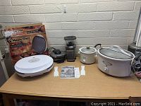 Photo showing all kitchen items on a wooden table including the Magic Chef electric skillet, two slow cookers, food dehydrator, coffee grinder, two spatulas, and the electric skillet box.