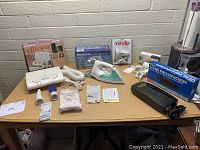 Full table view of assorted vintage household appliances and accessories with boxes.