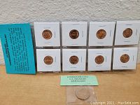 Front view of ten U.S. Treasury commemorative copper-colored medallions mounted in individual paper holders placed on a clear acrylic display stand, with a blue informational card visible.