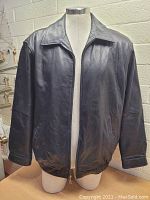 Front view of men's black leather jacket on a mannequin, showing zip closure and collar.