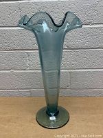 Front view of a tall blue glass vase with ruffled top and round base, showing shape and color.