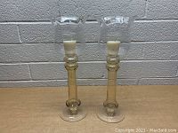 Front view of the pair of vintage glass candlesticks with amber stems, clear chimneys, and white candles inside.