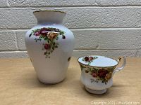 Royal Albert bone china white vase with floral designs in red and yellow, alongside matching teacup featuring the same floral pattern and gold trim.