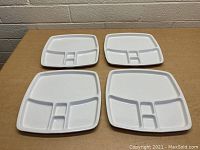 Four white stoneware compartment plates arranged on a table, showing their shape and divisions.