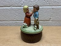 Front view of vintage boy and girl rotating music box on a green grassy base and brown textured base