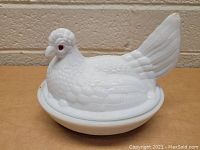 Side angle view of milk glass hen dish showing textured feathers and red glass eyes