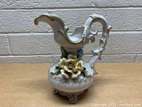 Side view of cream-colored vintage pitcher with ornate curved handle and detailed 3D yellow rose decoration on body, standing on four decorative feet.