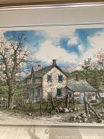Framed print showing a stone farmhouse with rustic fence and trees under blue sky with clouds.