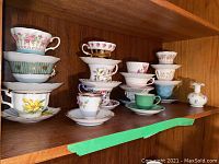 All teacups stacked with matching saucers on wood shelf showing collection variety and condition