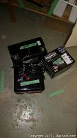 Photo showing large black battery and boxed Eliminator charger with cables on floor