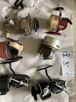 Top view of all six fishing reels, showing various colors and designs on a white background with lot tag visible.