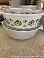 Two white Pyrex casserole dishes stacked with glass lids, featuring a green geometric pattern on the top dish.