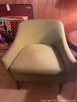 Green upholstered mid-century modern style chair with curved arms and backrest, shown from front angle.