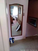 Full-length wooden framed mirror mounted on a wall, showing partial room reflection with carpeted floor and furniture.