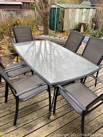 Full view of rectangular glass top patio table with six chairs around it on wooden deck.