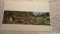 Panoramic landscape print showing nature scene with trees, rocks, a river, and mountain background, with a female figure included in the composition.