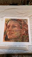 Full view of the square art print showing the woman's face formed by natural scenes, laid flat on a bed.