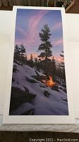 Full view of vertical limited edition print showing snowy landscape with campfire and pine trees under colorful sky, on white border background.