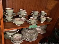 Shelf displaying many pieces of china including cups, saucers, plates, creamer, sugar bowl.