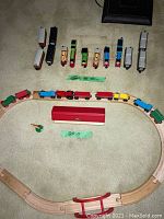 Full view of Brio wooden train set with track assembled in oval shape and a collection of 10 Thomas the Tank Engine trains lined up.