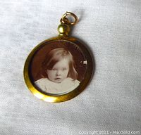 Front side of the pendant showing sepia photo of a young child, with gold tone circular frame and glass protection.
