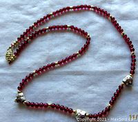 Full view of the garnet bead necklace with three enamelled cloisonné heart beads and gold accents laid flat.