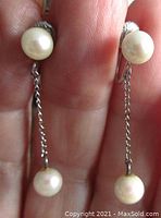 Close-up front view of mid-century sterling silver cultured pearl drop earrings held between fingers showing white round pearls attached at top and bottom connected by a silver chain.