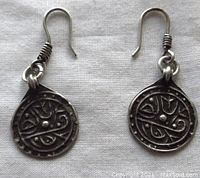 Pair of round drop earrings made in old Turkoman ethnic style with embossed calligraphic design in sterling silver and darkened patina, wire hooks with coil detail.