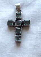 Top view of the sterling silver cross pendant showing six square blue faceted stones in a cross arrangement.