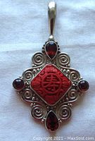 Front view of the pendant showing red cinnabar centerpiece, four garnets and sterling silver swirl design.