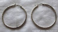 Pair of large sterling silver hoop earrings shown flat on white fabric background for size and texture visibility.