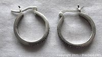 Pair of silver hoop earrings with marcasite on one side and a smooth finish on the other, laying flat on a white cloth background.