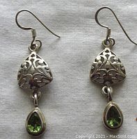 Front view of pair of sterling silver earrings with openwork design and green teardrop stones.