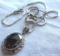 Top angle view of pendant and chain on white fabric background, showing the faceted black stone and marcasite surrounding details.